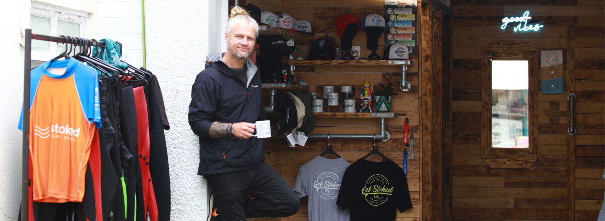 Julian, holding a stoked mug, standing in front of the Stoked Surf School