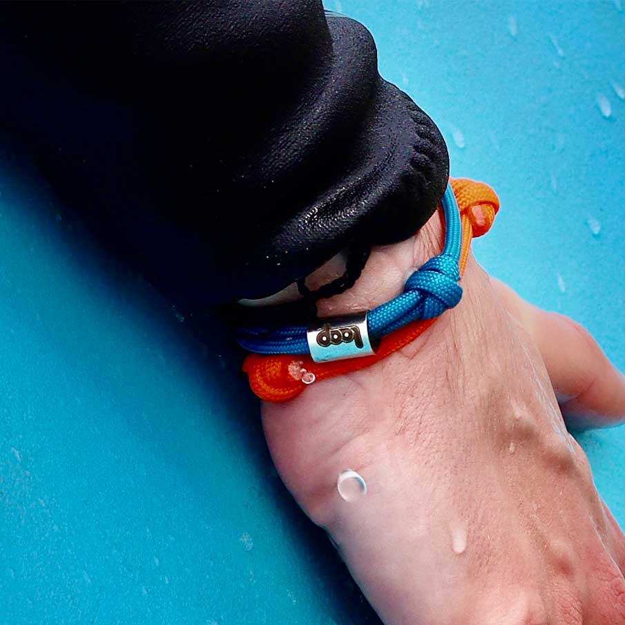 A hand holding a surfboards, with the Blue and Orange Loop bands on their wrist