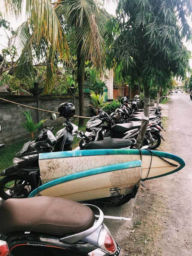 A broken surfboard, strapped to the side of a motorbike