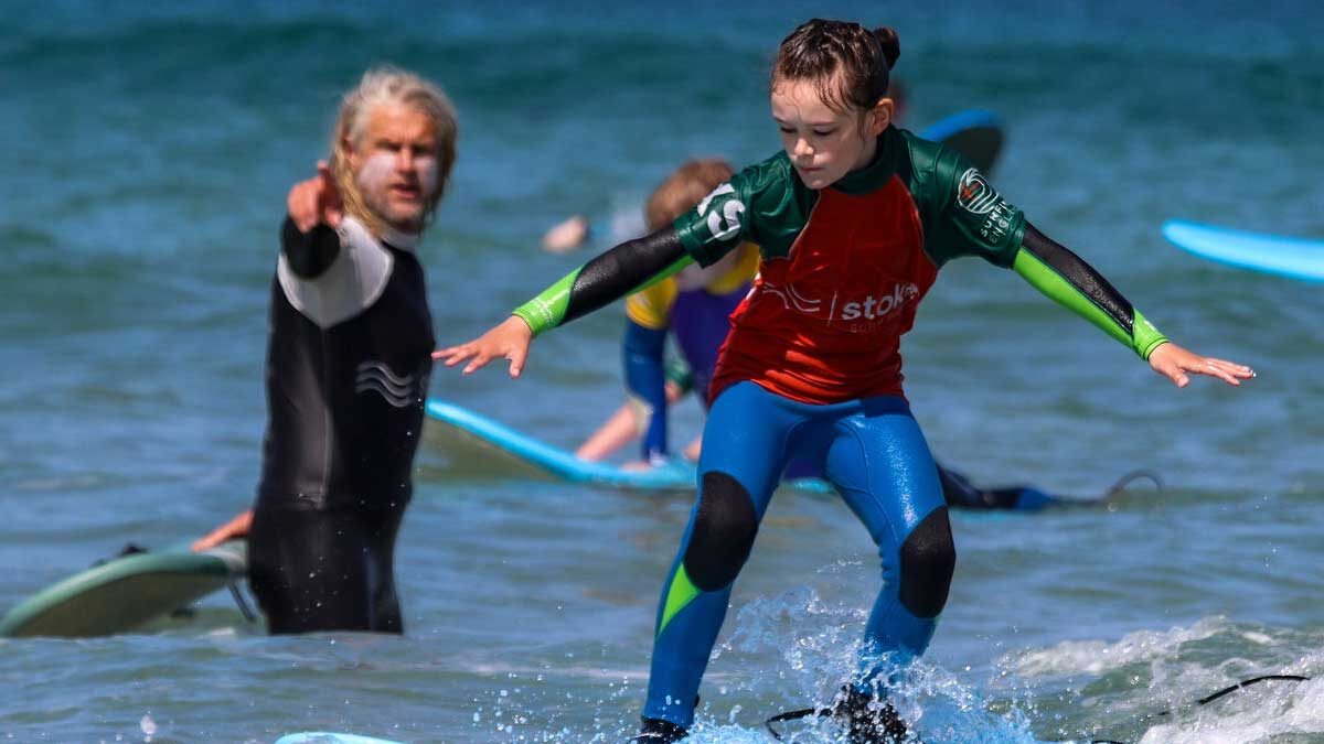 A young member of the Grom Squad, riding a wave as head coach Julian watches