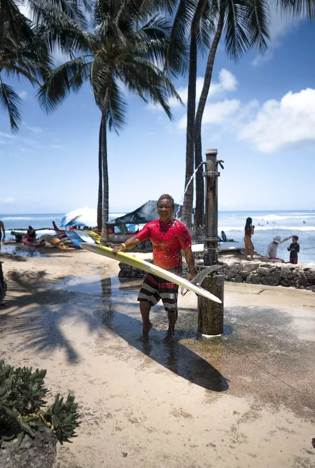 A man washing himself and his surfboard after a surf