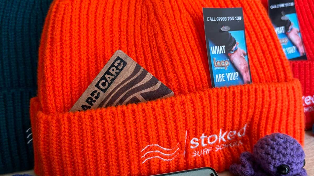 An orange Stoked beanie hat with a Pard Card tucked into the band