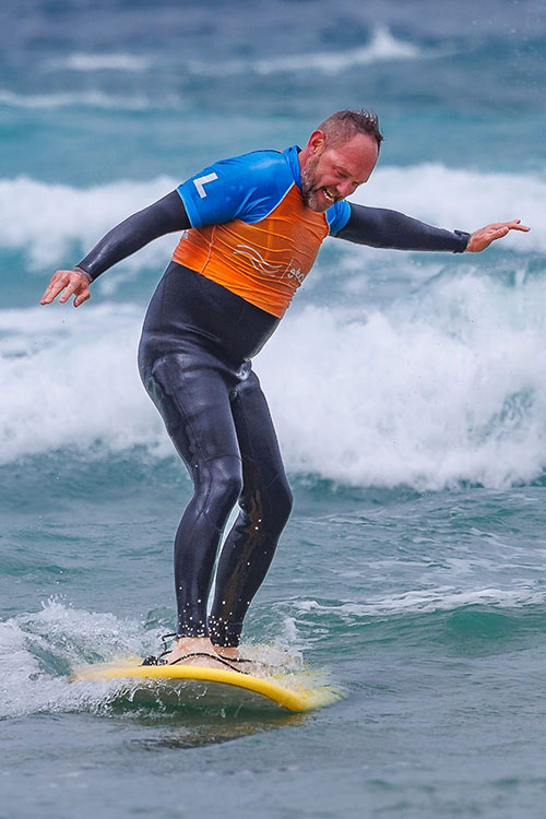 An older man standing on his surfboard, smiling