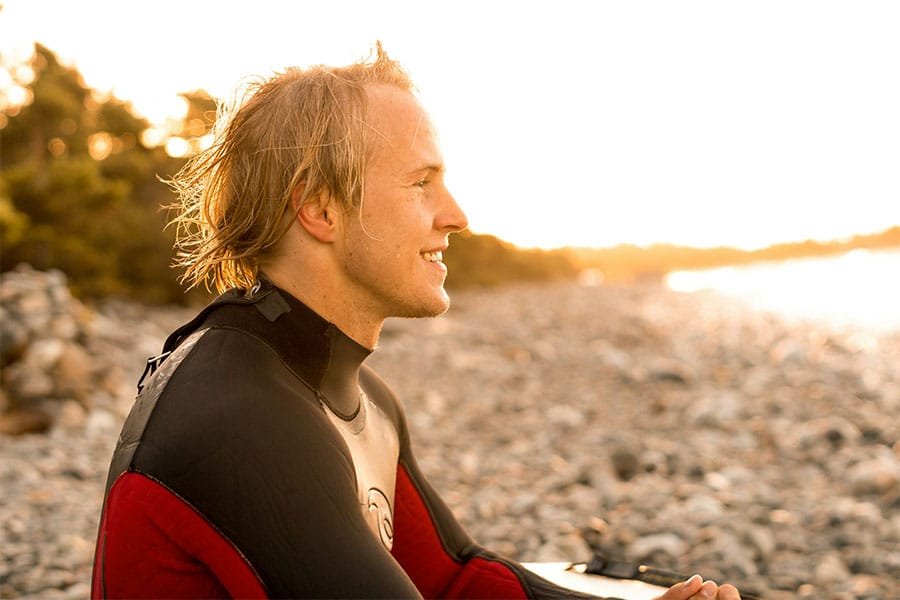 A surfer sat on a beach, smiling