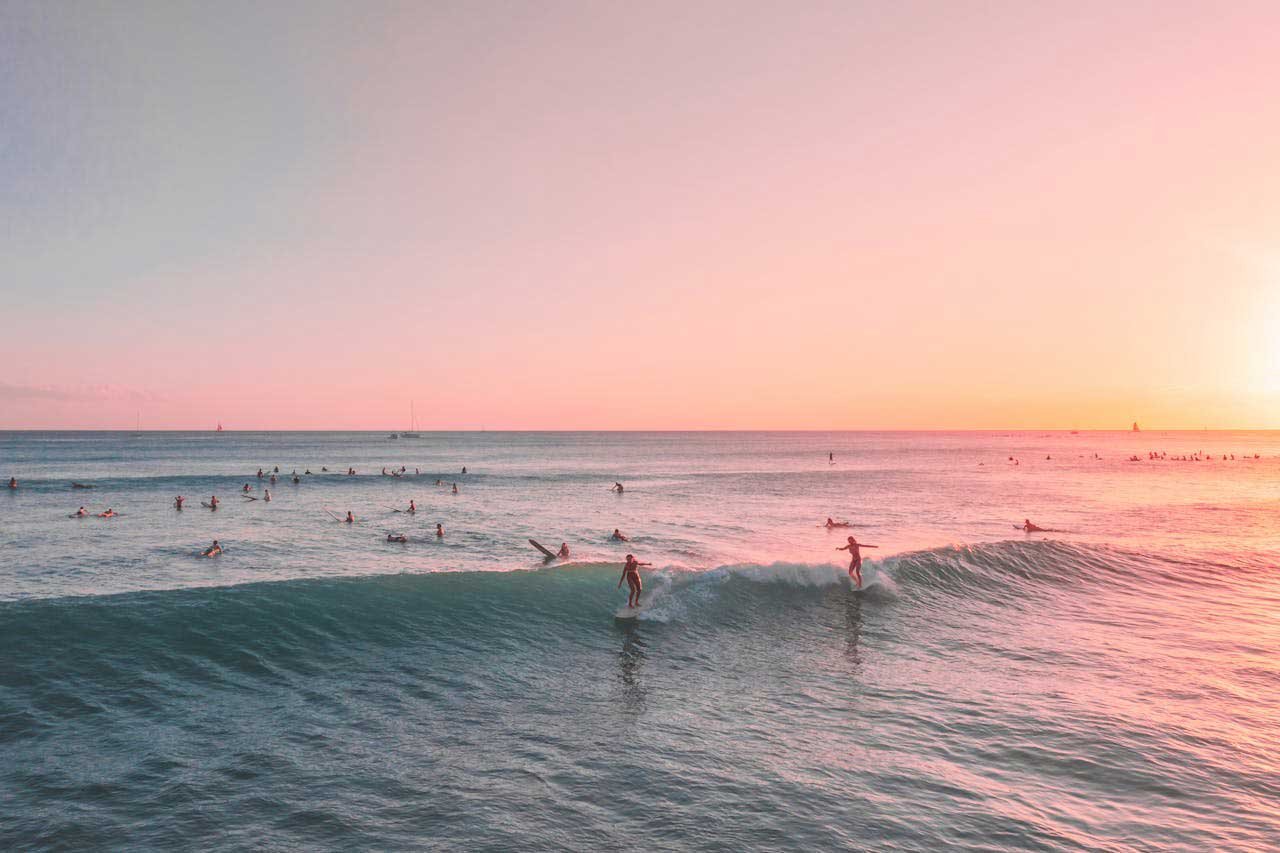 2 people happily riding a wave together at sunset