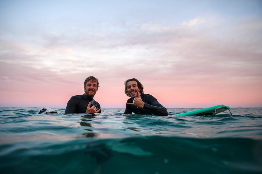 2 surfers throwing shakas and smiling in the water