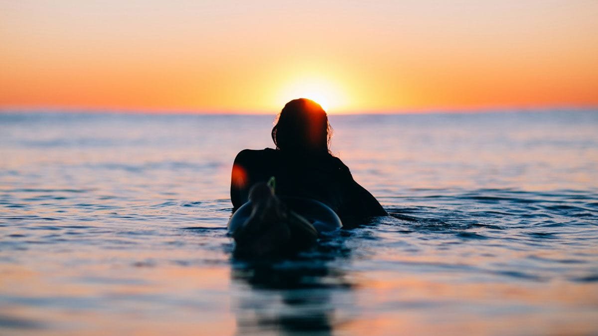 A surfer staring at the sunset whilst in the water