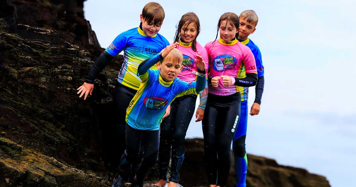 A group of young surf students, Stoked Surf School's "Grom Squad", jumping into the rock pool on Perranporth Beach