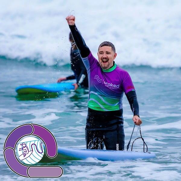 A smiling Stoked Surf School student with their fist raised to the air having progressed through the Loop Surf Ability Measure system and earning their purple loop