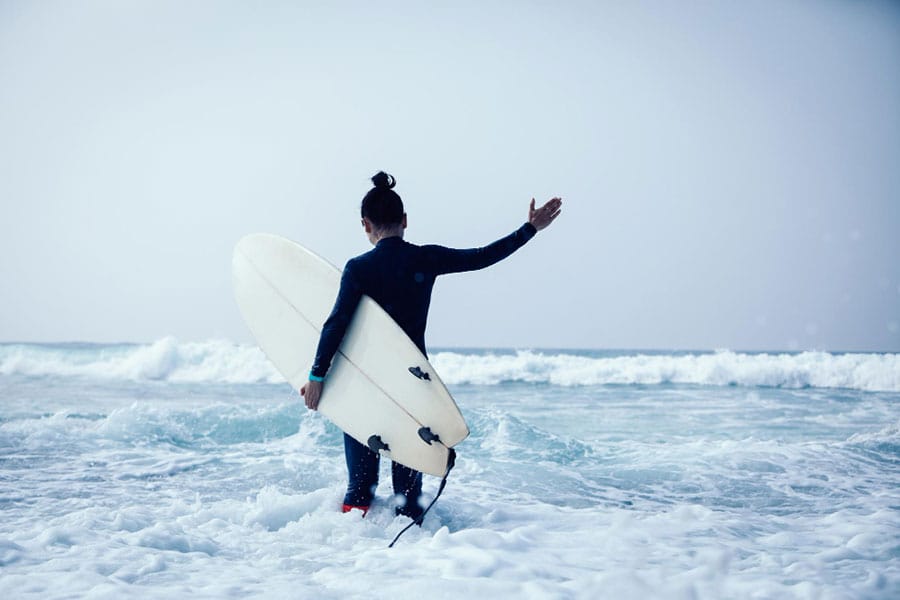 A man heading into the sea with a surfboard during winter