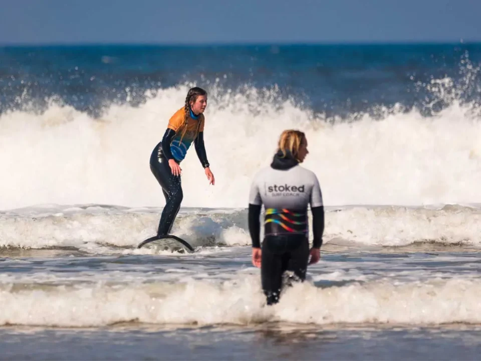 A woman riding a wave on Perranporth Beach with Stoked Surf School