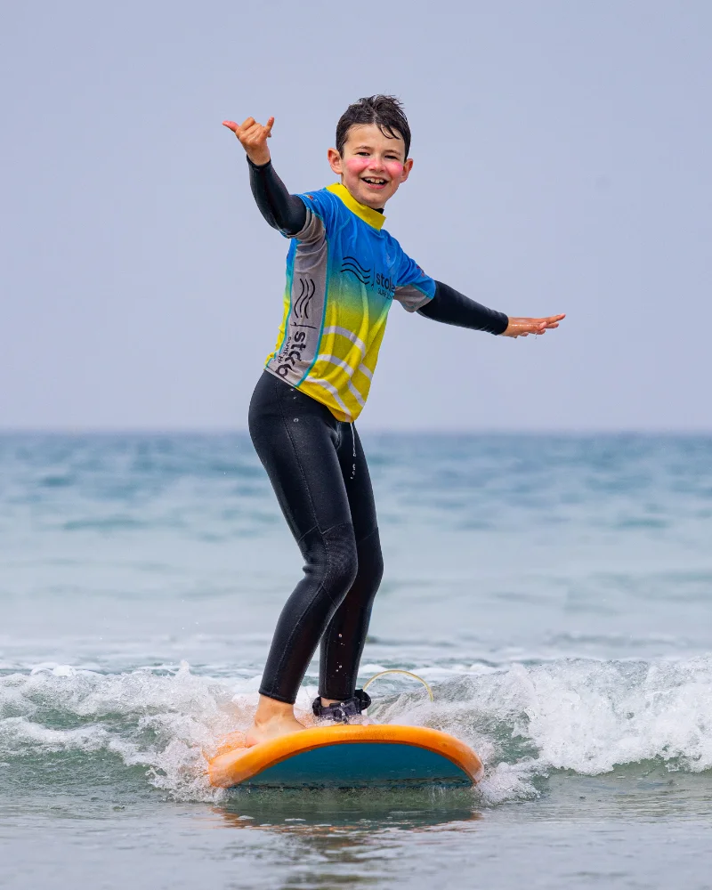 A young child smiling whilst riding a wave on a surfboard