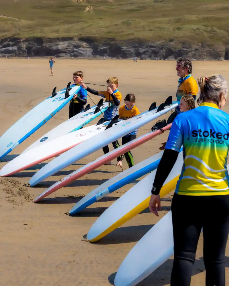 A group of people holding surf boards standing on Perranporth beach during a surf lesson