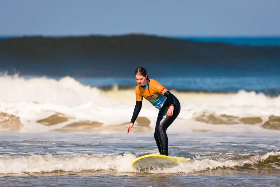 A beginner standing up and riding the white water on their first surf lesson